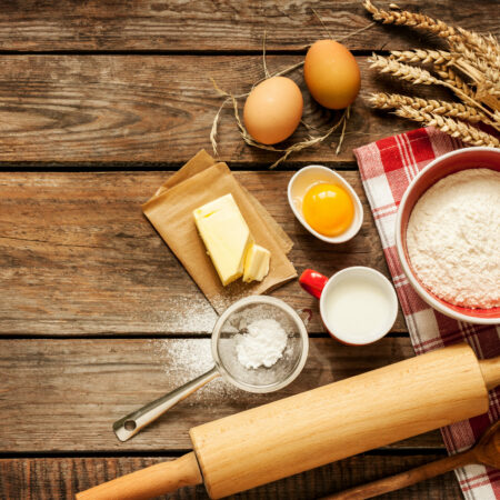 Baking cake in rural kitchen - dough recipe ingredients (eggs, flour, milk, butter, sugar) on vintage wooden table from above. Background layout with free text space.